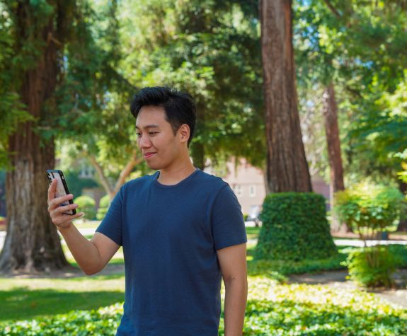 Image of male student looking down at phone and smiling.