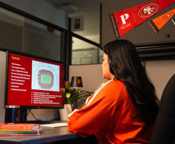 a student sits at a computer with 49ers gear around her