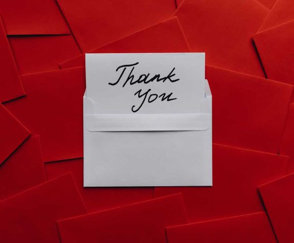 note card that says "thank you" sticking out of a white envelope on top of a bunch of red envelopes. Source: https://www.pexels.com/photo/card-on-top-of-red-envelopes-7430715/