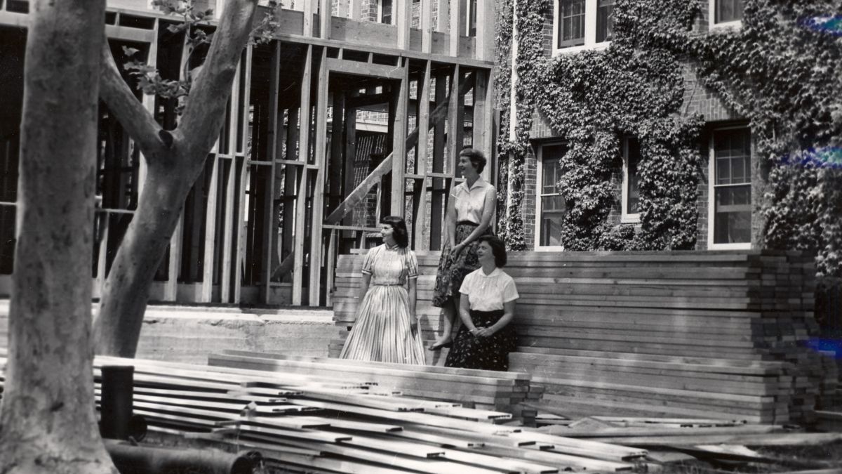 Several women stand near construction materials for West Hall