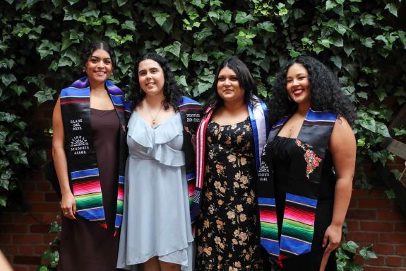Four students posing for a picture with graduation sash.