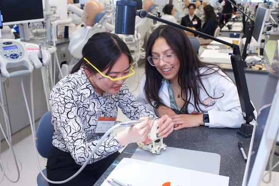 two women at a desk with one of them holding a drill and a typodont