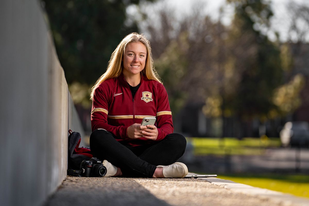 college student wearing a sport jersey sits on a soccer field