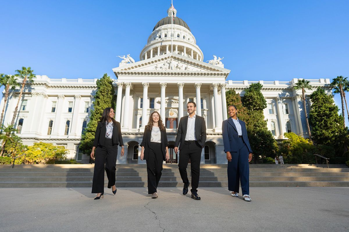 Four individuals walking in business attire in front of the Sacramento Capitol building. 