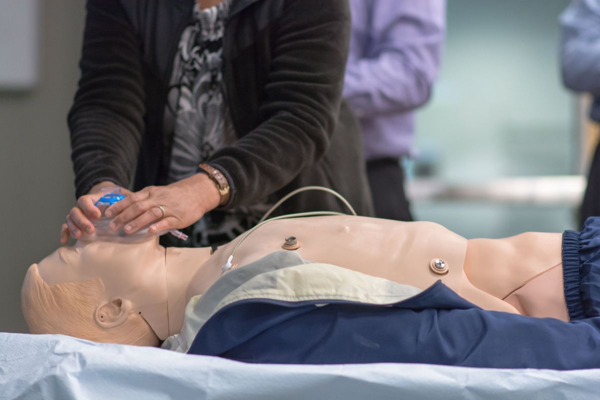 Photo shows a student standing next to a manikin while practicing putting on a breathing mask. 