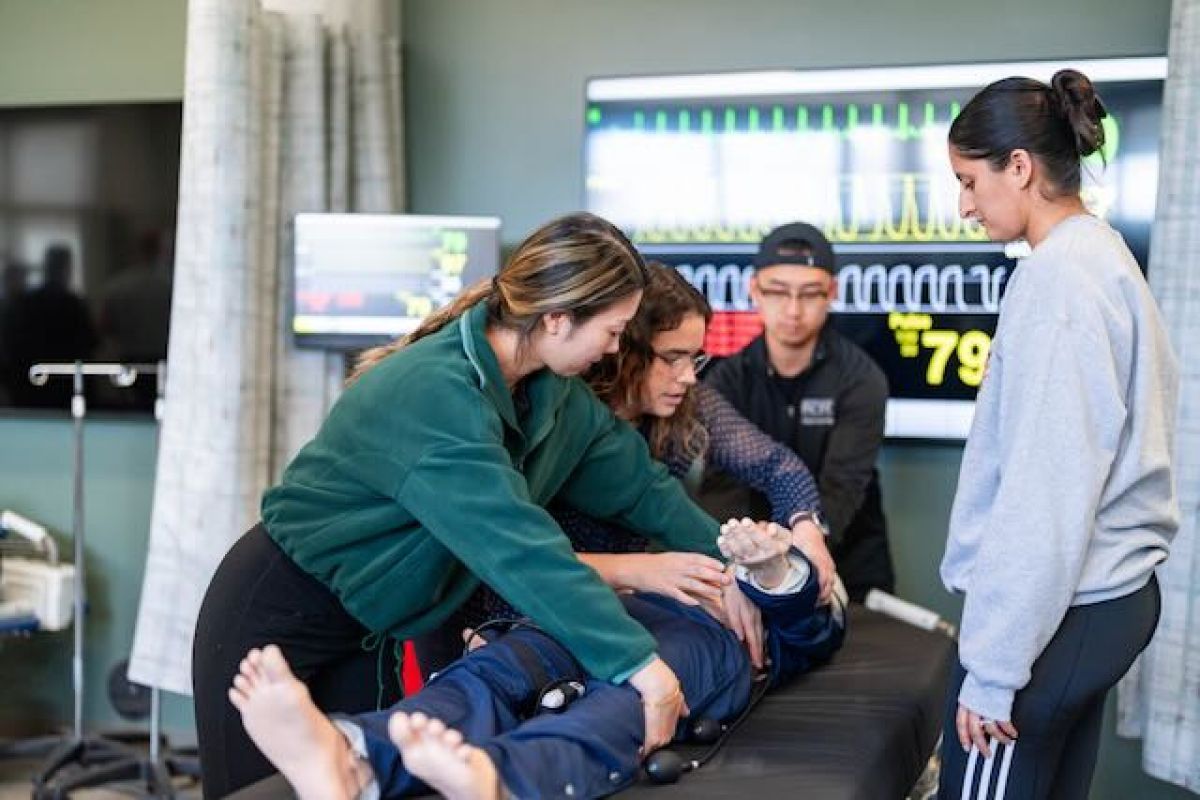 Image shows three students being instructed on a procedure on a mannequin