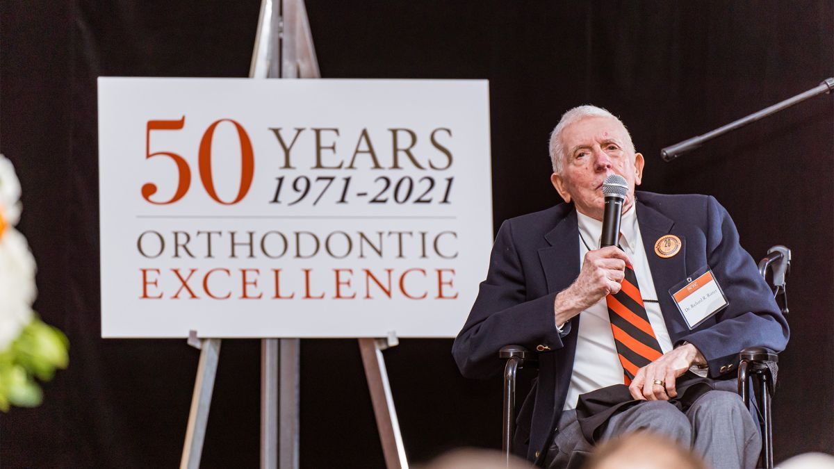 Richard Rutter sits in a chair next to a sign that reads 50 years of orthodontic excellence 