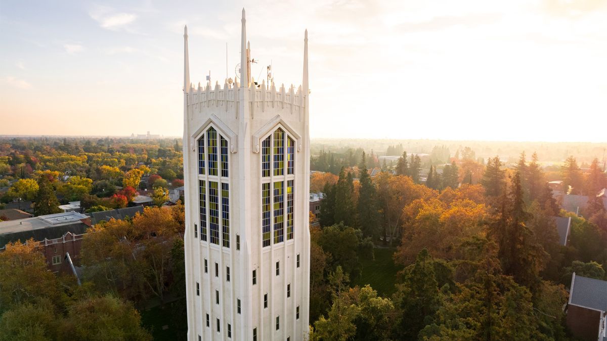 An aerial image of a tall white tower in front of fall foliage