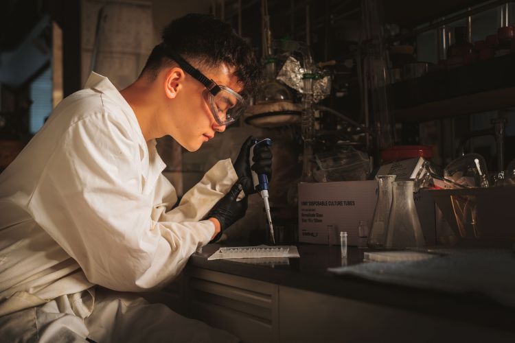 student in lab coat works over lab table