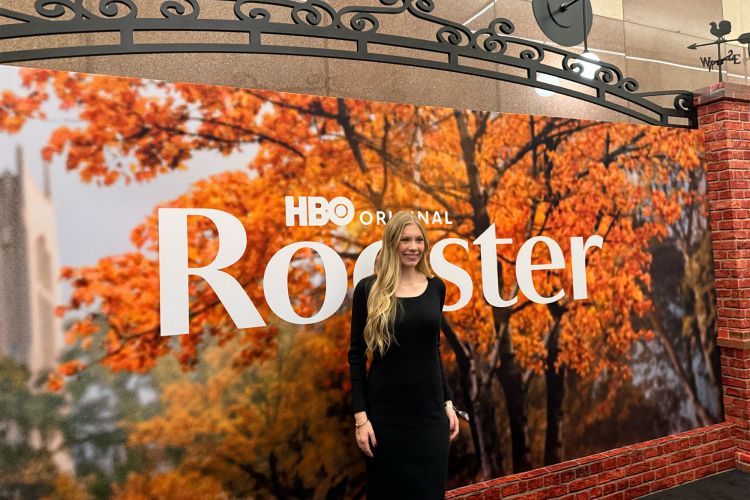 a student stands in front of a large poster with word 'Rooster'