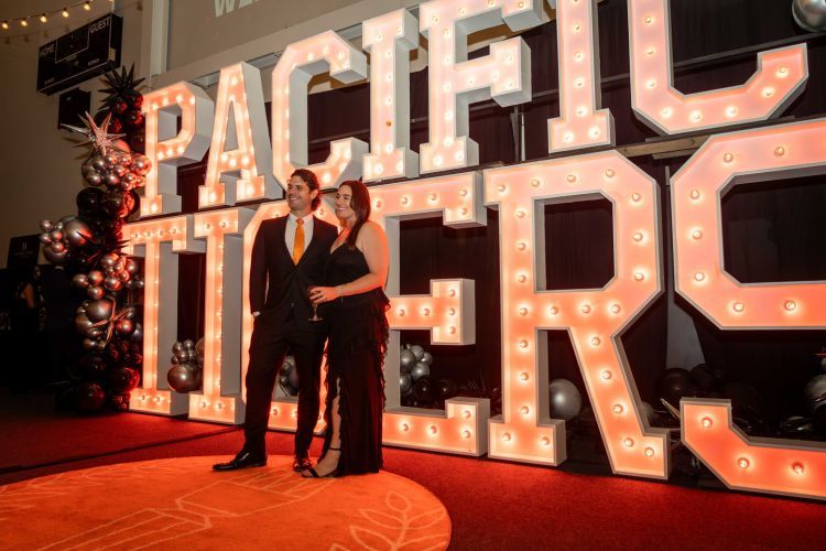 Two people dressed in black in from of a Pacific Tigers sign