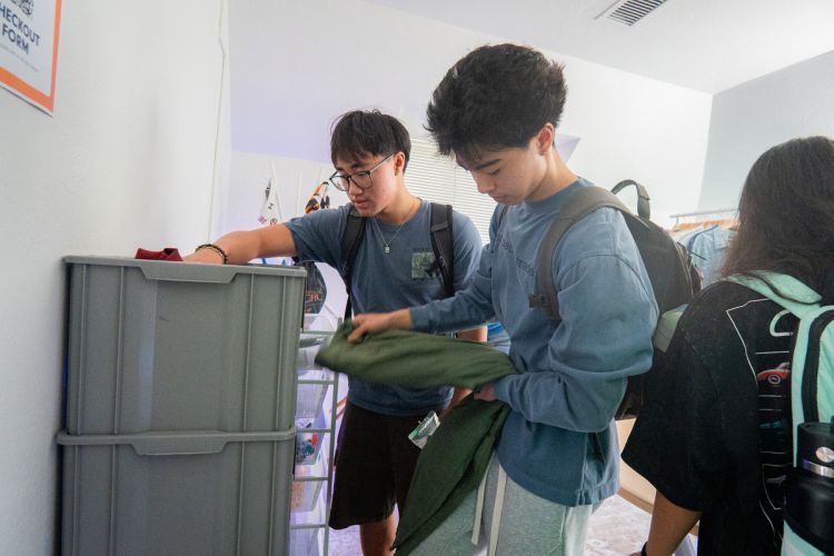 two students stand next to a rack holding a shirt