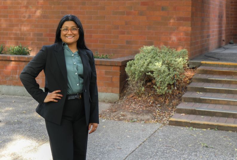 A woman wearing a suit poses for a photo outdoors on a campus