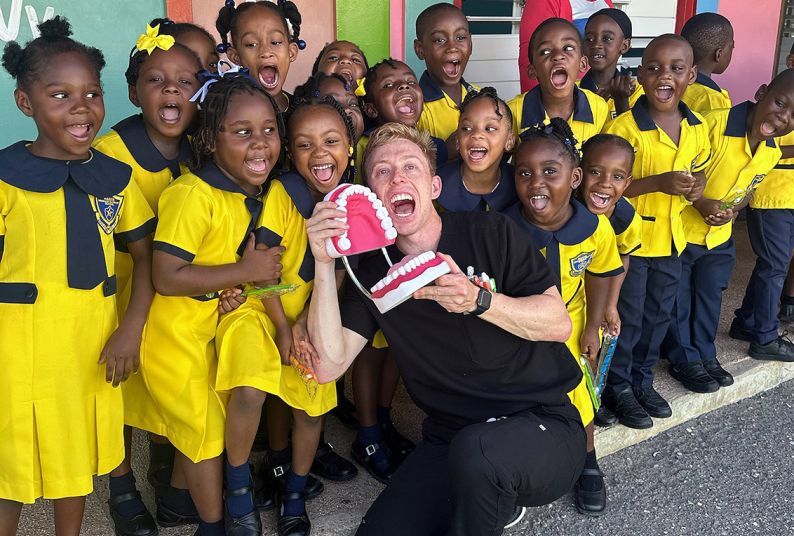 male dental student holding large plastic jaw for teaching the group of children posed with him