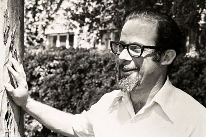 A man wearing glasses stands next to a tree