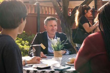 Professor Jeff Hole sits at a table outside with two students.