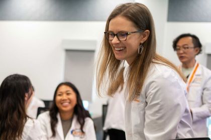 A faculty member in a lab coat smiling in the foreground.