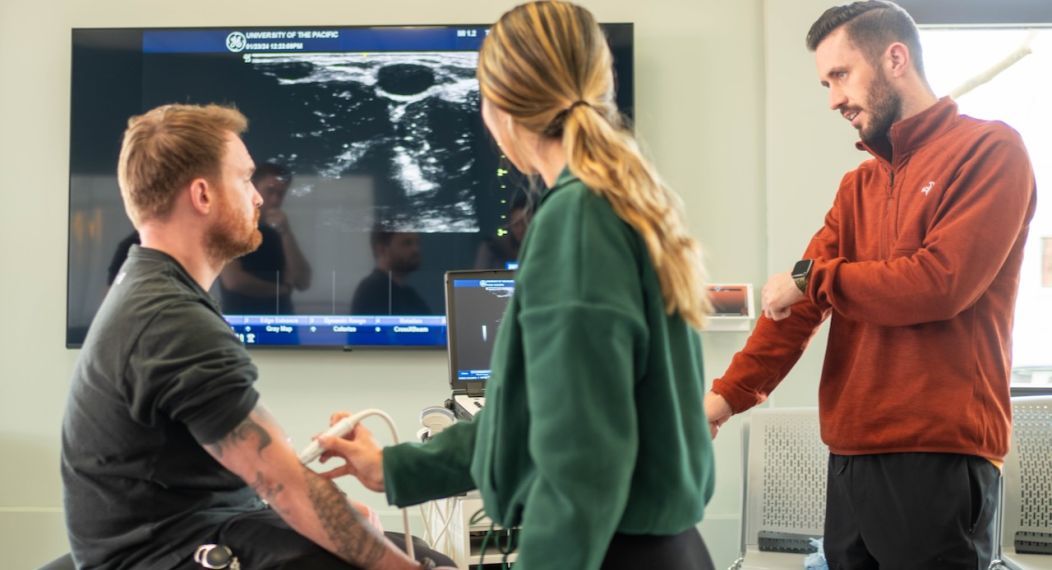 Photo shows three PA students practicing using diagnostic equipment.