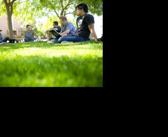 students sitting on campus lawn with professor