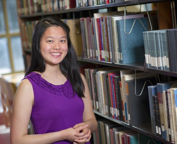 Scholarship winner smiles in library stacks.