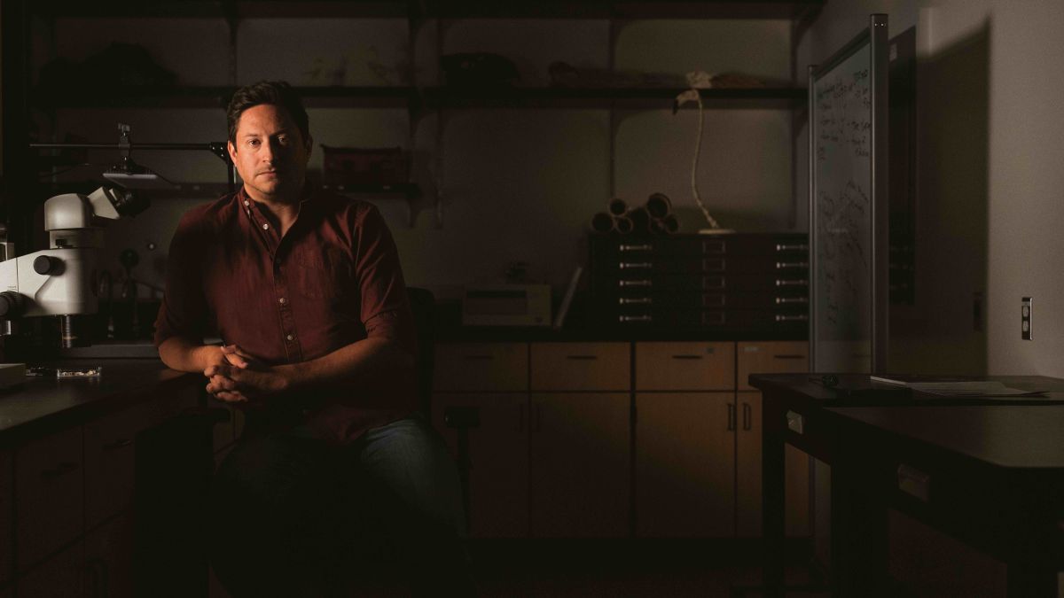 a man sits at a desk in a lab, looking at the camera
